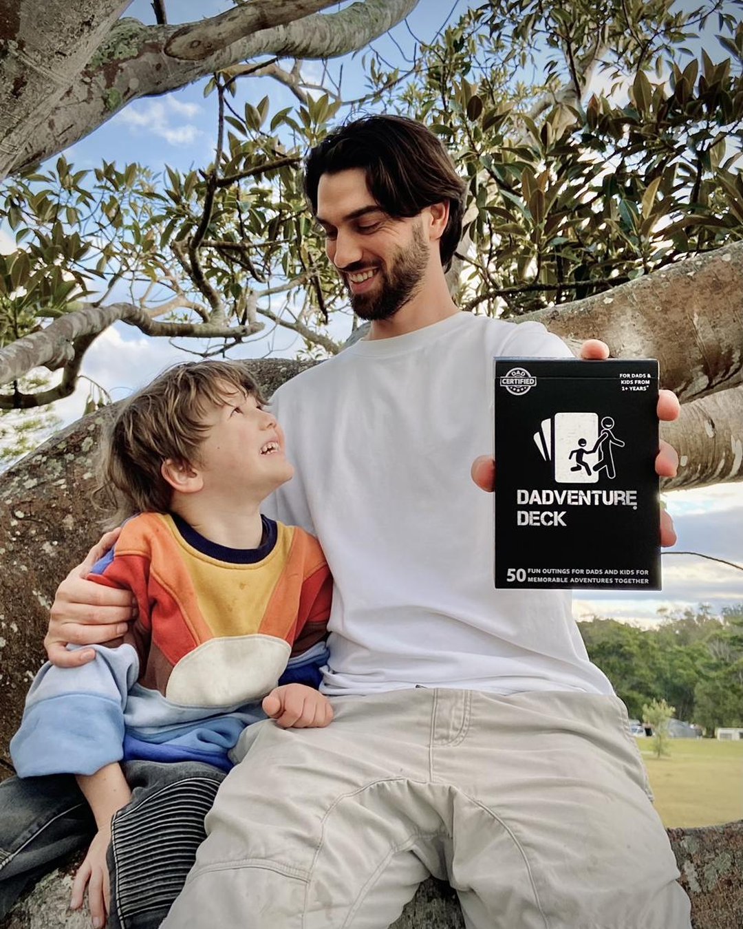 A dad and his son in a tree holding the Dadventure Deck